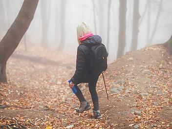 Eine geheimnisvolle Frau wandert allein auf einem Waldweg, umhüllt von dichtem Nebel, der eine unheimliche und mystische Atmosphäre schafft. A mysterious woman walks alone on a forest trail, enveloped by thick fog, creating an eerie and mystical atmosphere