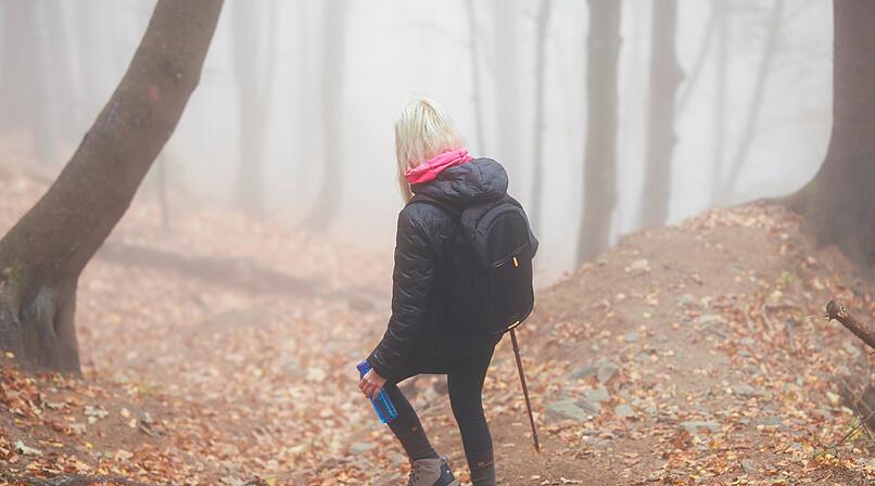 Eine geheimnisvolle Frau wandert allein auf einem Waldweg, umh&uuml;llt von dichtem Nebel, der eine unheimliche und mystische Atmosph&auml;re schafft. A mysterious woman walks alone on a forest trail, enveloped by thick fog, creating an eerie and mystical atmosphere