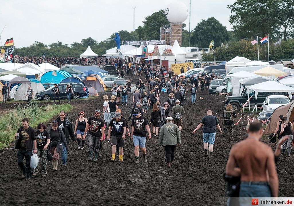 Metal-Fans laufen am 04.08.2016 in Wacken (Schleswig-Holstein) auf dem Gelände des Wacken Open Air durch den Matsch.