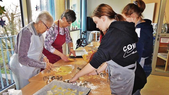Mit F&ouml;rmchen stechen Heimbewohnerin Christa Linke (links) und M&auml;dels der Klasse 7cM aus dem ausgerollten Butterteig Sterne, Tannenb&auml;ume und andere weihnachtliche Motive aus. Hauswirtschaftslehrerin Waltraud Fischer (Zweite von links) leitet die Backaktion im Seniorenzentrum.