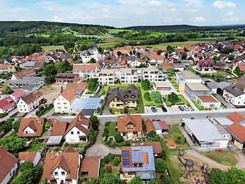 Rund um das gelbe Mehrfamilienhaus in der Bildmitte soll ein attraktives Zentrum entstehen: rechts das Bibliotheksgebäude mit Veranstaltungsraum und Café, links die teilweise überdachte Zufahrt zur Tiefgarage unter der Wohnanlage. Dazwischen ein kleiner Park und entlang der Fabrikstraße neue Parkplätze. Das Projekt liegt zwischen Kirche und Rathaus sowie der Kindertagestätte St. Anna: Pettstadts neue Mitte könnte so aussehen.  Fotomontage: Tschopoff/Grafik & Layout