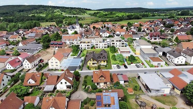 Rund um das gelbe Mehrfamilienhaus in der Bildmitte soll ein attraktives Zentrum entstehen: rechts das Bibliotheksgebäude mit Veranstaltungsraum und Café, links die teilweise überdachte Zufahrt zur Tiefgarage unter der Wohnanlage. Dazwischen ein kleiner Park und entlang der Fabrikstraße neue Parkplätze. Das Projekt liegt zwischen Kirche und Rathaus sowie der Kindertagestätte St. Anna: Pettstadts neue Mitte könnte so aussehen.  Fotomontage: Tschopoff/Grafik & Layout