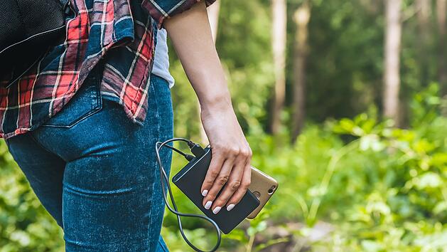 Power bank in a girl s hand, against the background of the forest and greenery Powerbank in der Hand eines M&auml;dchens, vor dem Hintergrund des Waldes und des Gr&uuml;ns.Wandern