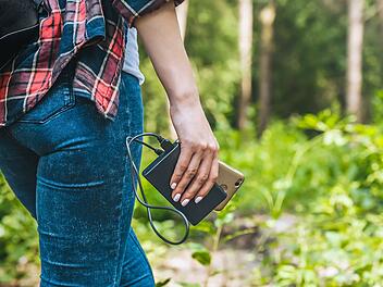 Power bank in a girl s hand, against the background of the forest and greenery Powerbank in der Hand eines Mädchens, vor dem Hintergrund des Waldes und des Grüns.Wandern