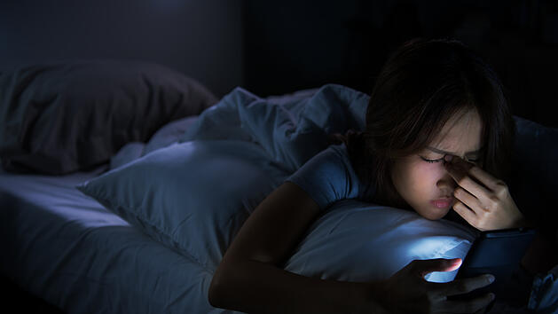Frau mit Handy im Bett kann nicht einschlafen.