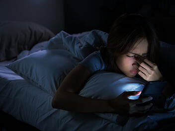 Frau mit Handy im Bett kann nicht einschlafen.