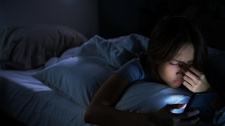 Frau mit Handy im Bett kann nicht einschlafen.