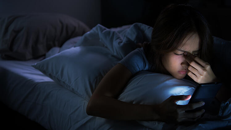 Frau mit Handy im Bett kann nicht einschlafen.