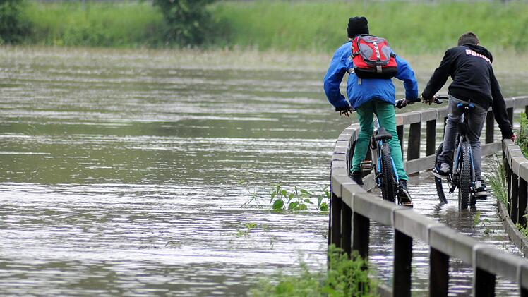 Vom Hochwasser nicht aufhalten lassen haben sich diese beiden Jungs in Fürth. Sie fahren trotz der Fluten mit ihren Rädern über einen Steg, der über eine Wiese führt. Foto: News5/Ott
