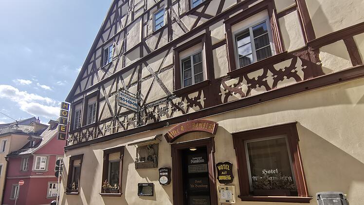 Fachwerkgebäude mit Hotelbeschilderung. Ein Schild weist auf das "Restaurant Poseidon" hin. Die Straße ist gepflastert und das Wetter wirkt sonnig und klar.