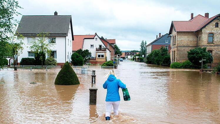 Ein Frau versucht am 26.07.2017 in Rhüden (Niedersachsen), einem Stadtteil von Seesen, durch das hohe Wasser zu gehen. Dauerregen hat im südlichen Niedersachsen in einigen Orten zu Überschwemmungen geführt. Foto: Hauke-Christian Dittrich/dpa