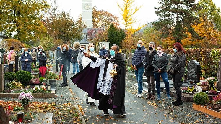 Coronamaßnahmen drücken auch dem Allerheiligen-Gottesdienst ihren Stempel auf: Die Gläubigen stehen mit Maske an den Gräbern ihrer Lieben, während Pfarrvikar  James Nangachveetill den Segen erteilt.    Benedikt Döring