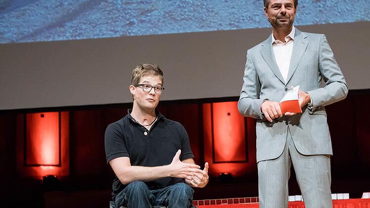 Als Felix Brunner die 800 Blutspenden erwähnt, erstarren die Gesichter der 458 geladenen Blutspender aus Unterfranken. Diese Menge hatte der junge Mann benötigt, als er 2009 bei einem Unfall beim Bergsteigen 30 Meter in die Tiefe stürzte. Jetzt konnte er seinen Lebensrettern danken. Rechts Moderator Michael Sporer.