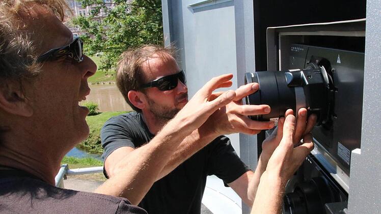 Olaf Kasprzyk (von links) und Claus Rau montieren die Objektive der beiden Beamer im hochwassersicheren und klimatisierten Gehäuse. Foto: Ralf Ruppert