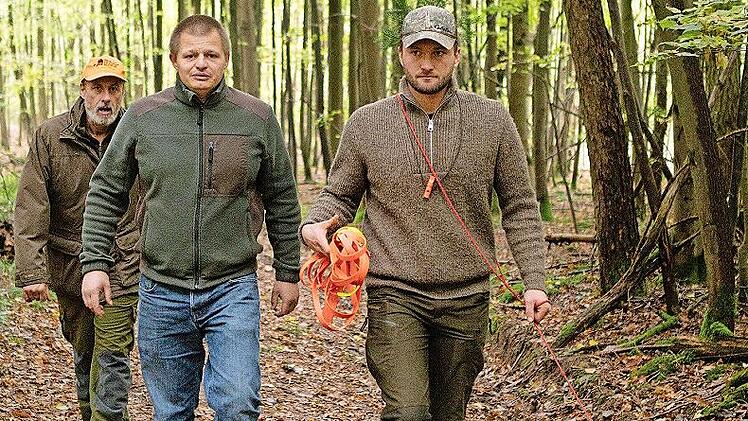 Der Hund arbeitet die Schweißfährte am sogenannten Schweißriemen. Die Prüfer begleiten die Suche.