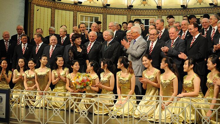 Getümmel am Ende des Konzerts: Die Damen und Herren des Studentenchores der Universität Peking und die Herren des Landkreismännerchors Bad Kissingen applaudieren einander. Mit auf der Bühne sind Chorleiterin Prof. Hou Xijin, Bad Kissingens 2. Bürgermeister Prof. Dr. Dr. Peter Deeg (Mitte) und der Präsident des Fränkischen Sängerbundes, Peter Jacobi (im grauen Anzug). Foto: kdc