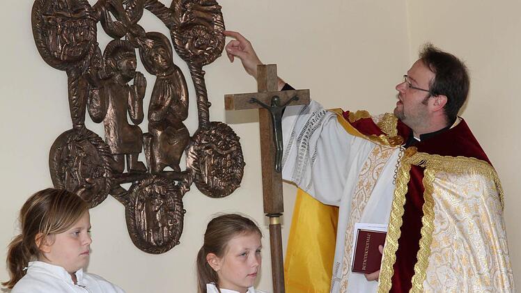 Pfarrer Daniel Schuster erklärt die Darstellungen auf dem Bronzerelief, das an der Drosendorfer Aussegnungshalle einen neuen Standort gefunden hat.  Foto: Erlwein