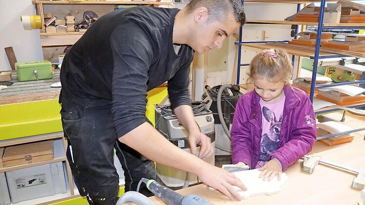 Die kleine Lena Ruderich (6 Jahre) fertigt mit Hilfe von Azubi Nikolas Deinhart ihr eigenes Brotzeitbrettchen in Form eines Schweinchens aus Ahornholz und Augen aus Buche. Foto: Andrea Spörlein