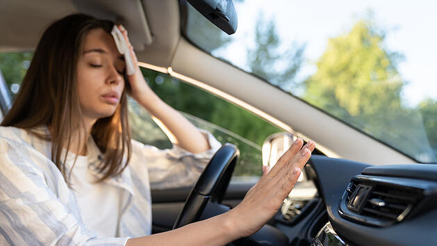 Eine Autofahrerin hat ein Problem mit einer nicht funktionierenden Klimaanlage, die Hand prüft den Kaltluftstrom, ihr ist während der Hitzewelle im Auto heiß, sie leidet unter dem heißen Sommerwetter und wischt sich mit einem Taschentuch den Schweiß von der Stirn. Weniger anzeigen, Klimaanlage macht krank