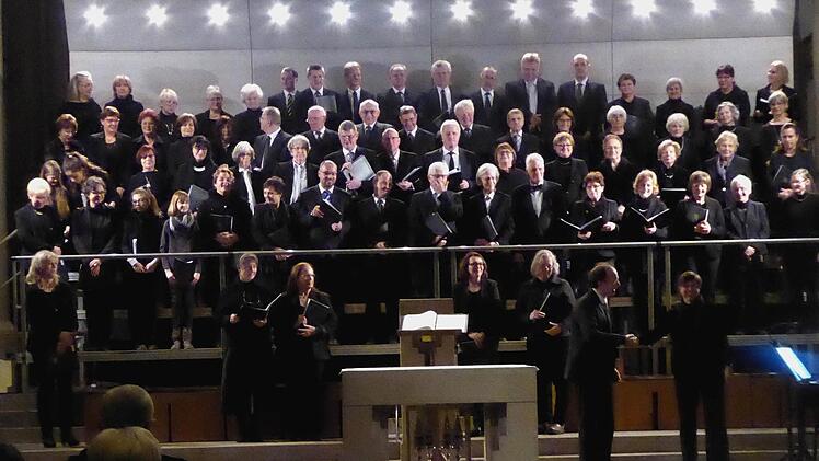 Alle drei Chöre präsentieren sich auf dem riesigen Chorgerüst hinter dem Altar der Herz-Jesu-Kirche mit ihrem Leiter Burkard Ascherl, Brigitte Ascherl (links) und ihrer musikalischen Unterstützung auf dem elektrischen Klavier, Ute Stibor (rechts) beim Schlussapplaus. Foto: Gerhild Ahnert