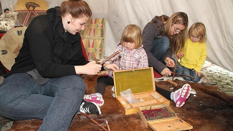 Im Inneren des Tipis ist es angenehm trocken und warm: Michaela Gabor, Lucie hoch (4), Sarah Milz und Sophie Milz (3) basteln Schmuck aus Specksteinen. Foto: Sonja Adam