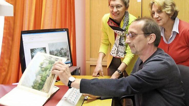 Peter Fenzel beim Digitalisieren des "Souvenir de Cobourg", einem Band mit aquarellierten Ansichten aus Coburg. Bibliotheksleiterin Silvia Pfister und Renate Bauer (von links) schauen über die Schulter.