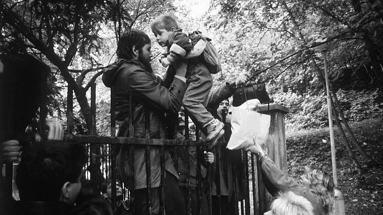 DDR-Bürger reichen Kinder über den Zaun der bundesdeutschen Botschaft in Prag. Hier warteten sie auf eine Einreisemöglichkeit in die BRD.  Foto: Reinhard Kemmether / dpa