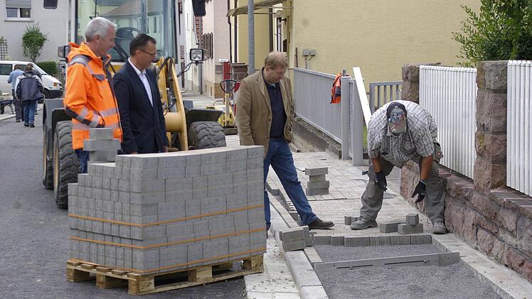 Der verbreiterte Gehweg kommt den Auraer Bürgern gelegen. Bauleiter Klaus-Peter Straub, Bürgermeister Thomas Hack und Baudirektor Jürgen Eisentraut betrachten die Arbeit des Pflasterers der Firma Hell.  Fotos: Winfried Ehling