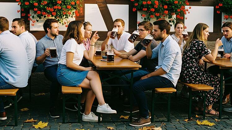 Ein paar Frauen und Männer im Alter zwischen 25 und 35 trinken im Spätsommer aus Krügen Bockbier vor einer fränksichen Brauereigaststätte. Einige trinken aber auch Wasser und Apfelschorle.