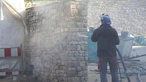 Ein Arbeiter strahlt die Bruchsteinmauer des Schlettenhofs ab.