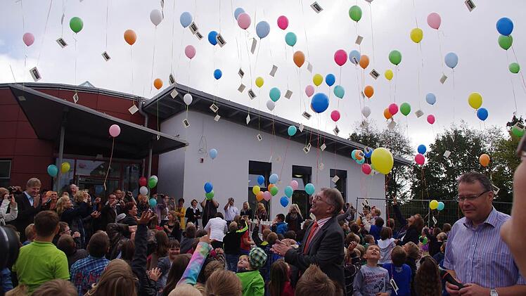 Kinder und Erwachsene lassen vor der Schule Luftballons steigen.