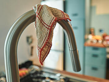 Checked dishcloth draped over a stainless steel kitchen faucet  von LoloStock