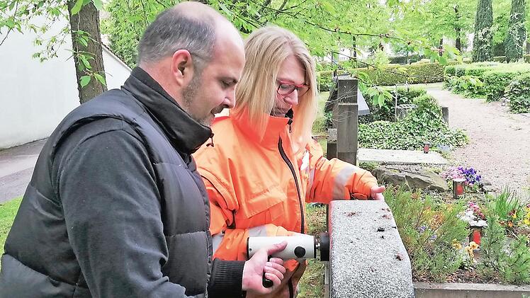 Friedhofsverwalter Stefan Krieg und Mitarbeiterin Carmen Goll pressen den Kipp-Tester an die Oberkante eines Grabsteins.