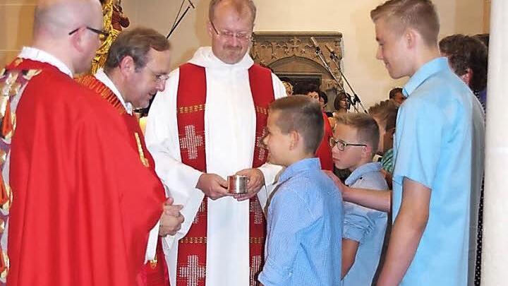 Christian empfängt durch Domkapitular Norbert Jung das Heilige Sakrament der Firmung. Mit auf dem Bild sind Kaplan Sven Raube (links) und Regionaldekan Thomas Teuchgräber (Mitte).  Foto: Heike Schülein