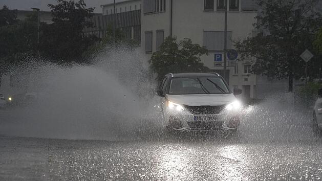 Ein Auto fährt bei starkem Regen auf einer überfluteten Straße. Foto: Andreas Rosar/dpa