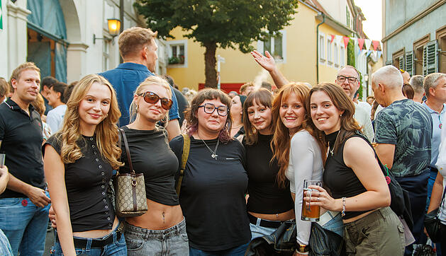 Eine Gruppe junger Frauen posiert l&auml;chelnd bei der Bamberger Sandkerwa. Sie stehen in einer belebten Stra&szlig;e voller Festivalbesucher. Einige halten Getr&auml;nke in der Hand.