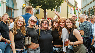 Endlich wieder Sandkerwa! Eine Gruppe junger Frauen posiert lächelnd bei der Bamberger Sandkerwa. Sie stehen in einer belebten Straße voller Festivalbesucher. Einige halten Getränke in der Hand.