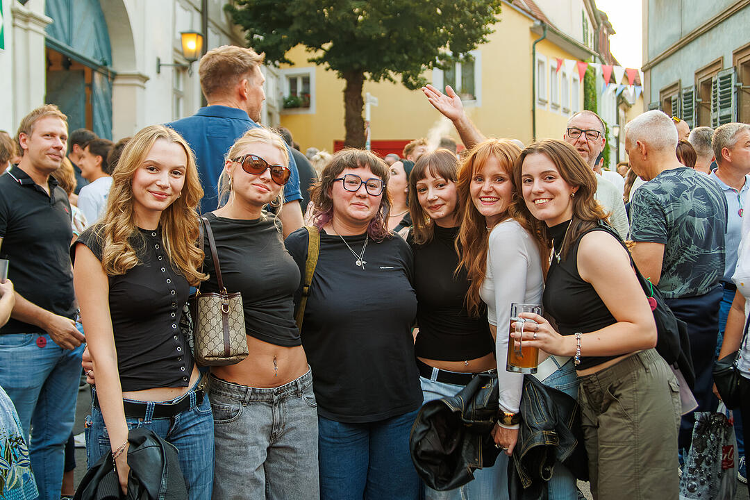 Eine Gruppe junger Frauen posiert l&auml;chelnd bei der Bamberger Sandkerwa. Sie stehen in einer belebten Stra&szlig;e voller Festivalbesucher. Einige halten Getr&auml;nke in der Hand.