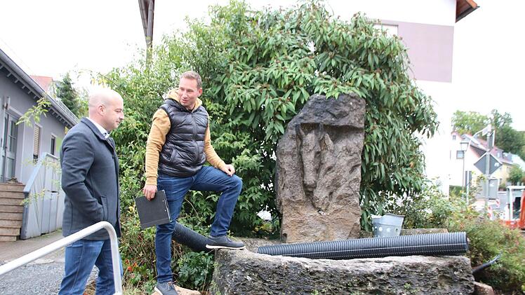 Bürgermeister Michael Kastl (links) und Ortsreferent Fabian Nöth im Gespräch am Reichenbacher Dorfbrunnen. Der erhält eine Wasserspielfläche. Versetzt werden muss er ohnehin. Foto: Thomas Malz.