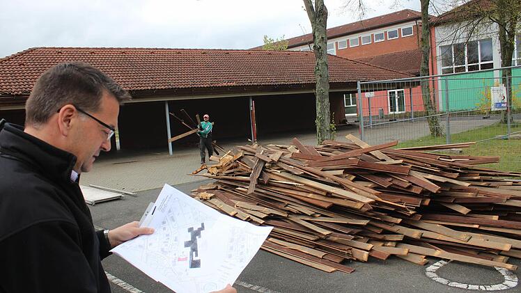 Bürgermeister Karsten Fischkal inspiziert den Lageplan für die neue Kinderkrippe, die an dieser Stelle auf dem Schulgelände entstehen soll. Um Platz für den Neubau zu schaffen, wurde mit dem Abriss der ehemaligen Fahrradhalle (im Hintergrund) begonnen. Foto: Andreas Dorsch