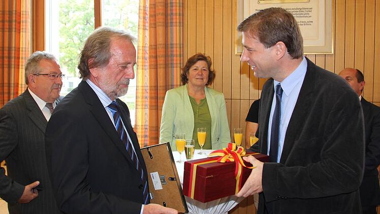 Landrat Hermann Ulm (rechts) überreicht Altlandrat Reinhardt Glauber die Urkunde und ein Geschenk. Im Hintergrund FW-Kreisrat Franz Schmidtlein und die Grüne Kreisrätin Edith Fießer. Foto: Roepert