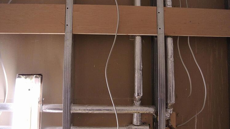 Hinter Trockenbauwänden verschwinden die notwendigen Installationen, sieht man hier in einem Elektroraum. Davor hängen doppelte Rigipsplatten. Wo, wie hier, später einmal Wandschränke hängen müssen, da wird mit Spanplatten verstärkt.