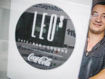 Probehalber hält Oleg Knoll einen Design-Entwurf für das neue Logo an die Glastür des Lokals. In der Spiegelung ist der Transporter der Handwerker zu sehen, die gerade die letzten Arbeiten verrichten.  Foto: Steffens