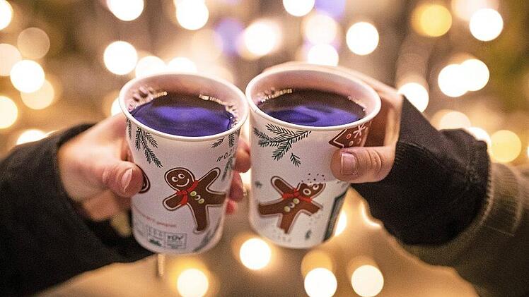 Zwei Frauen stoßen mit Glühwein gefüllten Bechern an. Statt auf dem Weihnachtmarkt trinkt man jetzt den Glühwein Zuhause. Dazu bestellt man Lebkuchen und Weihnachtsdeko im Internet. Foto: Christoph Schmidt, dpa