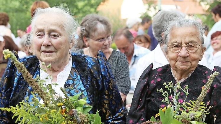 In Tracht und mit Würzbüscheln in der Hand nehmen diese zwei Frauen am Gottesdienst teil.