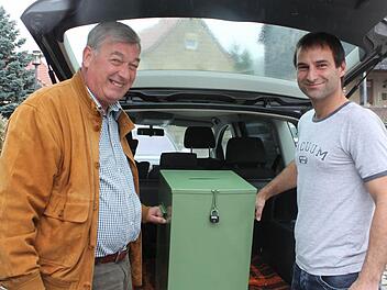 Werner Schneider und Markus Frank holen die wertvolle Fracht aus dem Kofferraum. Am Sonntagmittag fuhr Markus Frank die Wahlurne von Bischofsheim nach Sechsthal. Die beiden Orte teilen sich eine Urne, damit die Stimmzettel gemischt werden und das Wahlgeheimnis gewahrt wird. Fotos: Carmen Schmitt