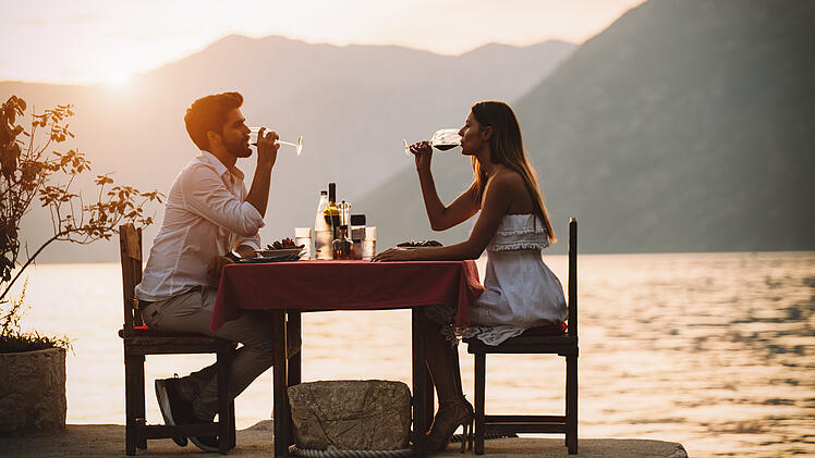 Ein Paar genießt ein privates Dinner-Event an einem tropischen Strand während des Sonnenuntergangs.