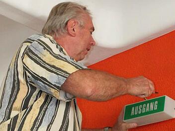 Hausmeister Franz Friedel ist montiert im Pfarrsaal das Notausgang-Schild. Foto: Mäuser