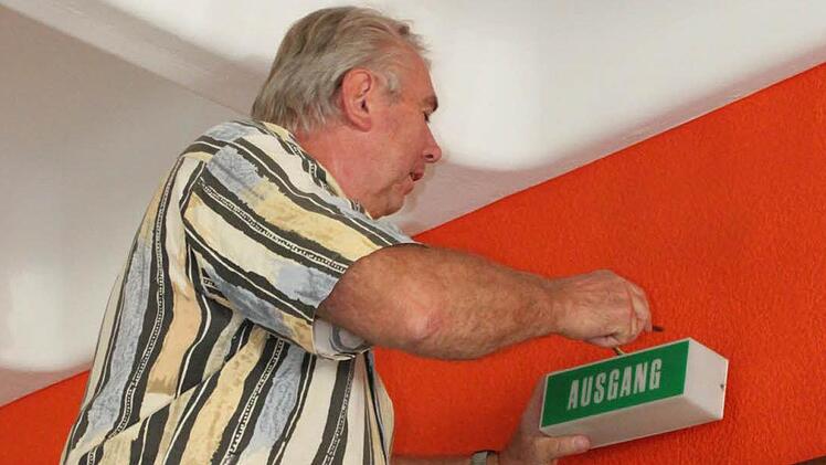 Hausmeister Franz Friedel ist montiert im Pfarrsaal das Notausgang-Schild. Foto: Mäuser