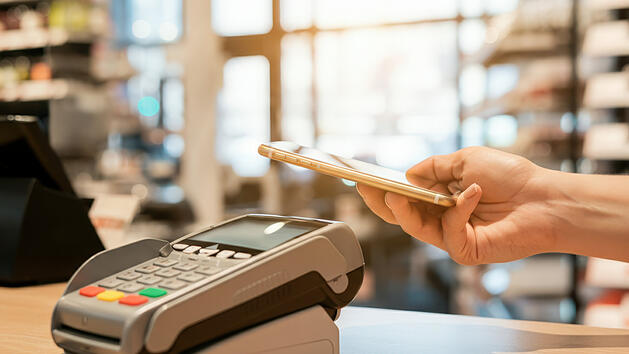 Ein Kunde hält sein Smartphone über ein Zahlungsterminal, um seinen Einkauf kontaktlos zu bezahlen, NFC